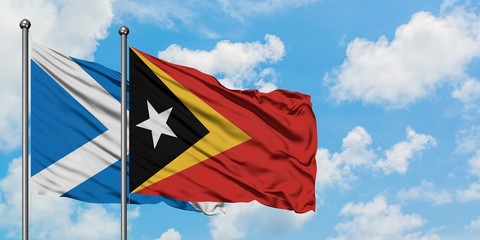 Scotland and East Timor flag waving in the wind against white cloudy blue sky together. Diplomacy concept, international relations.