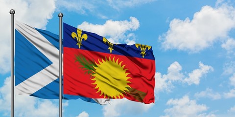 Scotland and Guadeloupe flag waving in the wind against white cloudy blue sky together. Diplomacy concept, international relations.
