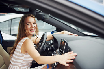 Leans on the steering wheel and smiling. Female driver inside of modern automobile. Testing brand...