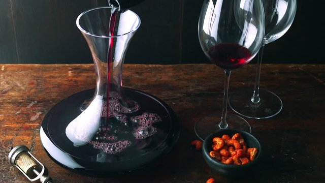 Rotwein wird neben Cashewn&uuml;ssen auf einem rustikalen Holztisch dekantiert