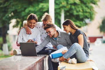 Concentrated at work. With laptop. Group of young students in casual clothes in the city at daytime