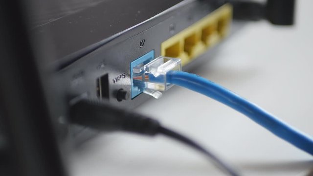 Man's Hand Plugging Blue Internet Cable In Wireless Router.