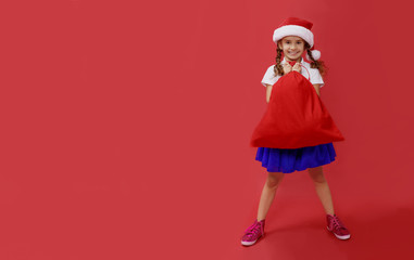 Horizontal view. Full-length portrait of a cute smiling little kid, holding a big red sack, over red background.