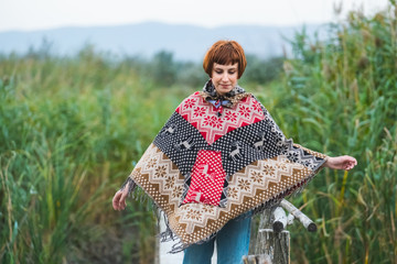 Young woman traveler dressed in a poncho walk outdoors in autumn fields