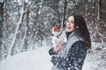 Look, it's snowfall. Smiling brunette having fun while walking with her dog in the winter park
