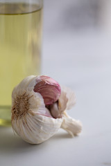 Ripe and raw garlic and garlic oil in glass of bottle on marble background