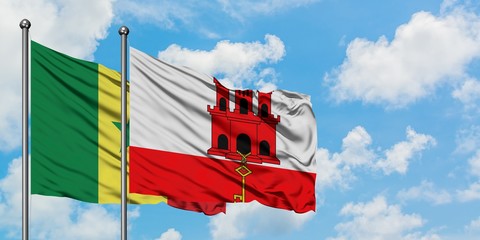 Senegal and Gibraltar flag waving in the wind against white cloudy blue sky together. Diplomacy...