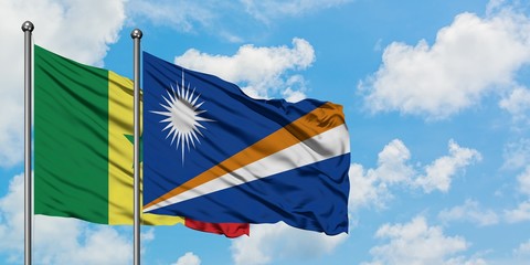 Senegal and Marshall Islands flag waving in the wind against white cloudy blue sky together....