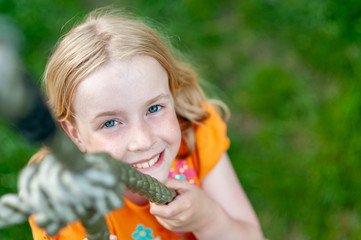 Top down shot of pretty young blonde girl smiling while climbing a rope. Focus on eyes, blurry background