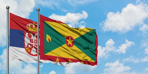 Serbia and Grenada flag waving in the wind against white cloudy blue sky together. Diplomacy concept, international relations.