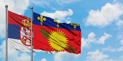 Serbia and Guadeloupe flag waving in the wind against white cloudy blue sky together. Diplomacy...