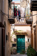 Fototapeta na wymiar Cozy courtyard with a green door, potted flowers, balconies with clothes in the Italian town of Cefalu, Sicily
