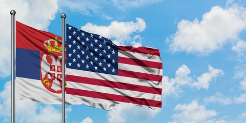 Serbia and United States flag waving in the wind against white cloudy blue sky together. Diplomacy concept, international relations.