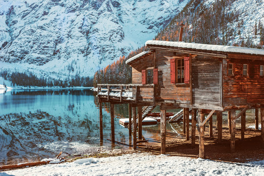 Wooden houses in the snow against the background of the crystal clear water of Lake Braies in the Dolomites, Italy. Colorful winter landscape in the snowy Italian Alps, a popular tourist spot in Italy