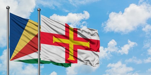 Seychelles and Guernsey flag waving in the wind against white cloudy blue sky together. Diplomacy...