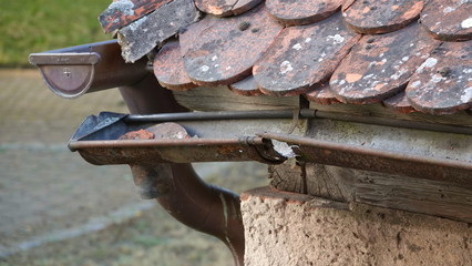 Badly damaged rain gutter on old tile roof