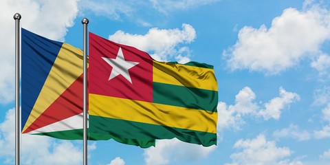 Seychelles and Togo flag waving in the wind against white cloudy blue sky together. Diplomacy...