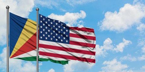 Seychelles and United States flag waving in the wind against white cloudy blue sky together....