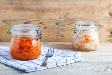 Korean carrots and fermented cabbage in glass jars on a wooden table