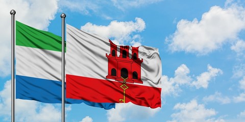 Sierra Leone and Gibraltar flag waving in the wind against white cloudy blue sky together....