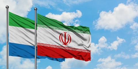 Sierra Leone and Iran flag waving in the wind against white cloudy blue sky together. Diplomacy...