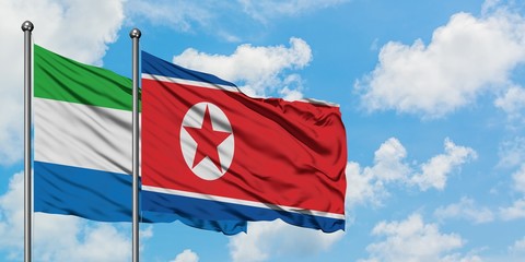 Sierra Leone and North Korea flag waving in the wind against white cloudy blue sky together....