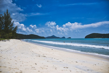 Waves of the azure Andaman sea under the blue sky reaching the shores of the sandy beautiful exotic and stunning Cenang beach in Langkawi island
