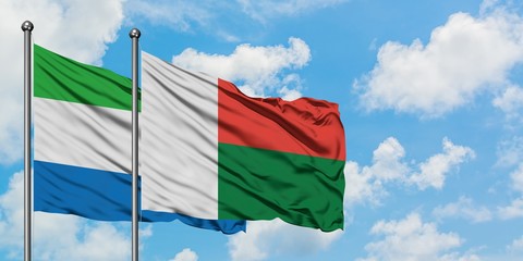 Sierra Leone and Madagascar flag waving in the wind against white cloudy blue sky together....