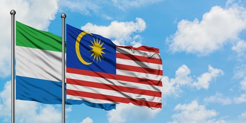 Sierra Leone and Malaysia flag waving in the wind against white cloudy blue sky together. Diplomacy...