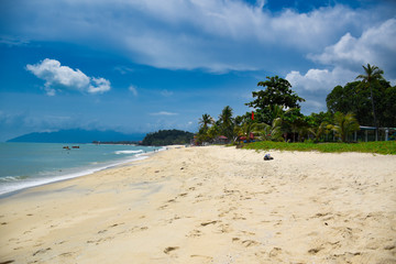 Waves of the azure Andaman sea under the blue sky reaching the shores of the sandy beautiful exotic and stunning Cenang beach in Langkawi island