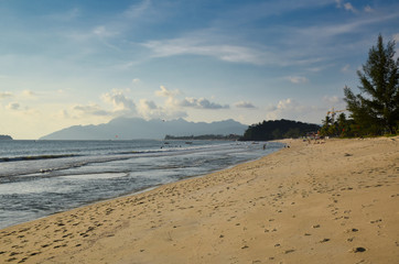 Waves of the azure Andaman sea under the blue sky reaching the shores of the sandy beautiful exotic and stunning Cenang beach in Langkawi island