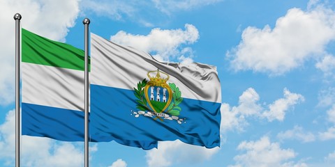 Sierra Leone and San Marino flag waving in the wind against white cloudy blue sky together....