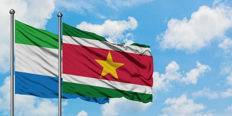 Sierra Leone and Suriname flag waving in the wind against white cloudy blue sky together. Diplomacy concept, international relations.