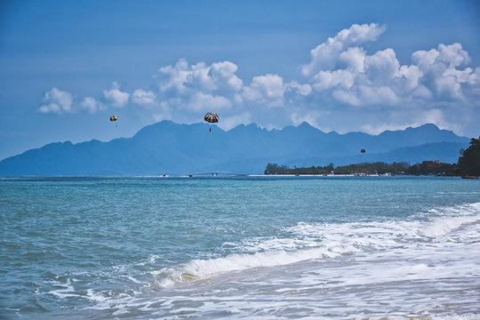 Parasailing on the waves of the azure Andaman sea under the blue sky near the shores of the sandy beautiful exotic and stunning Cenang beach in Langkawi island,