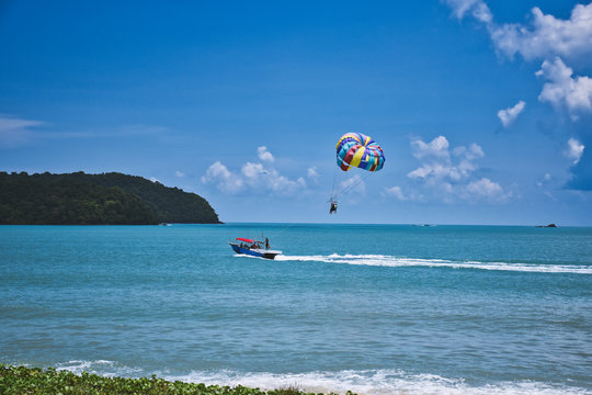 Parasailing on the waves of the azure Andaman sea under the blue sky near the shores of the sandy beautiful exotic and stunning Cenang beach in Langkawi island,