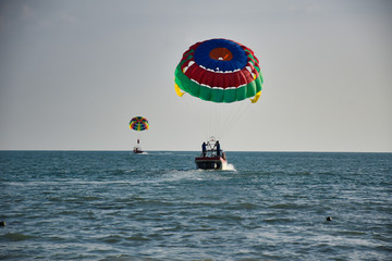 Parasailing on the waves of the azure Andaman sea under the blue sky near the shores of the sandy beautiful exotic and stunning Cenang beach in Langkawi island,