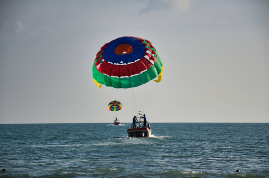 Parasailing on the waves of the azure Andaman sea under the blue sky near the shores of the sandy beautiful exotic and stunning Cenang beach in Langkawi island,