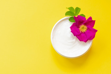 Fototapeta na wymiar White soft cream in a jar on bright yellow background with dog rose, top view, anti-ageing moisturizing cream with dog rose oil essential and vitamin E