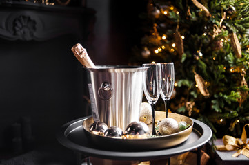 Champagne bottle in freezer bucket with glasses on dark background.