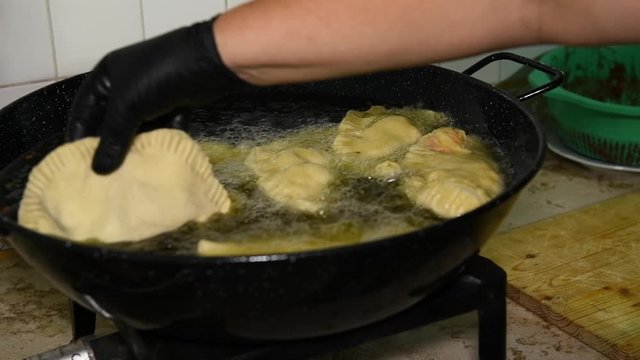 Frying Panzerotti. Female hands turn over apulian panzerotti patties, which are fried in olive oil in a large frying pan. Panzerotti is a traditional dish in Salento, Puglia, Italia