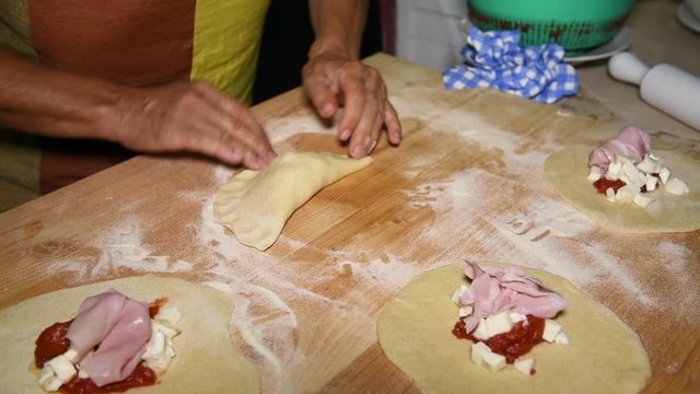 Feminine hands make Apulian panzerotti pies with tomato, mozzarella and prosciutto cotto. Panzerotti is a traditional dish in Salento, Puglia, Italy, fried in olive oil