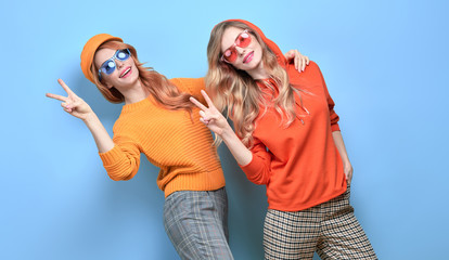 Two Lovable fashionable woman sisters dance in Trendy orange outfit. Studio shot of Carefree funny...