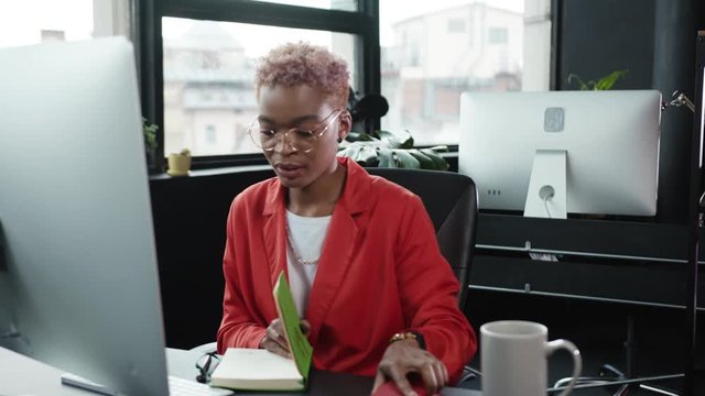 Black attractive businesswoman puts the phone down after client conversation typing keyboard at desktop computer working in the company.