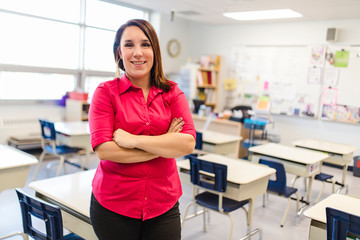 Pretty teacher smiling at camera at back of classroom at the elementary school