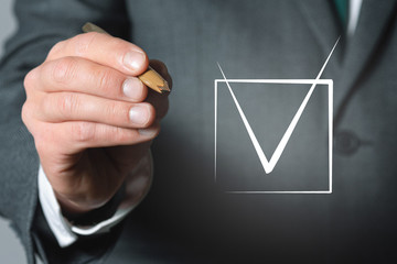 Tick in a checkbox and businessman hand with a ball pen close up background.