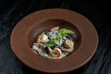 Black spaghetti with prawns on a black wooden table.