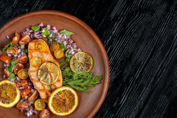 Grilled salmon and vegetables. Laid on a beautiful clay plate, sprinkled with onions, dill and tomatoes.
