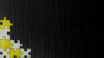 Silver and golden puzzle in the corner of the image on a black natural stone background of slate. A...