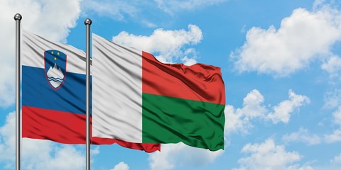 Slovenia and Madagascar flag waving in the wind against white cloudy blue sky together. Diplomacy...