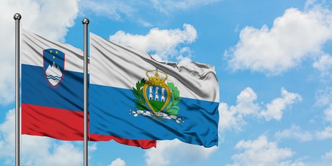 Slovenia and San Marino flag waving in the wind against white cloudy blue sky together. Diplomacy concept, international relations.